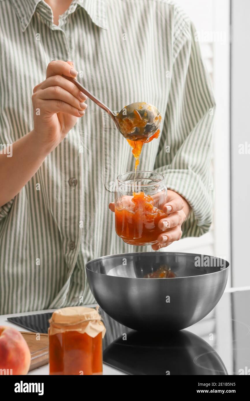 Donna che versa una gustosa marmellata di pesche dal recipiente nel recipiente Foto Stock