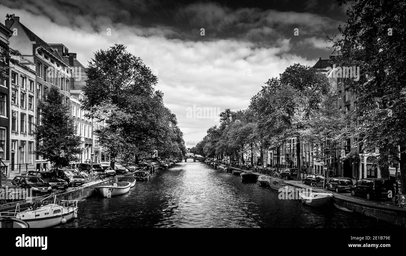 Foto in bianco e nero di piccole imbarcazioni, automobili e biciclette che costeggiano l'Herengracht, o canale dei signori, nel centro storico di Amsterdam, Paesi Bassi Foto Stock