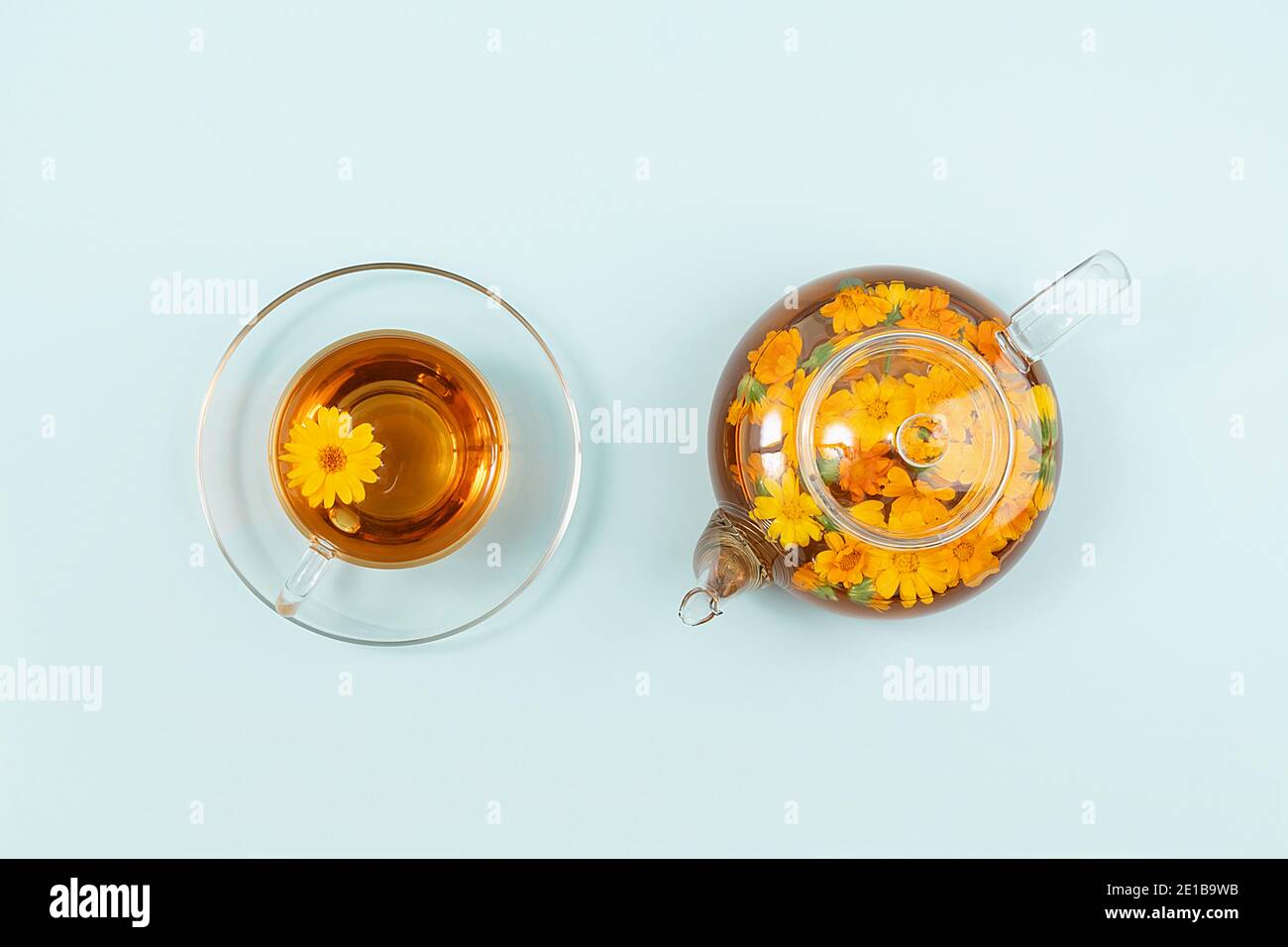 Tazza di tè alle erbe e teiera trasparente con fiori di calendula su sfondo blu. Calendula tè benefici il vostro concetto di salute. Vista dall'alto, disposizione piatta. Foto Stock