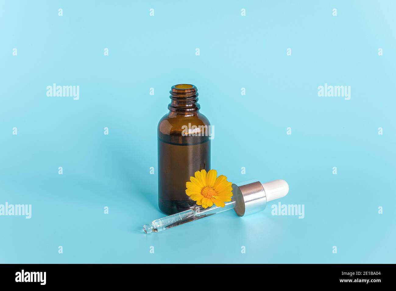 Olio essenziale in flacone contagocce marrone aperto con pipetta in vetro sdraiata e calendula con fiori arancioni su sfondo blu. Concept naturale biologico di bellezza cos Foto Stock