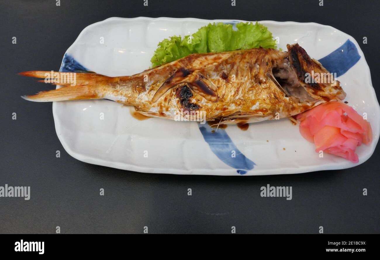Pesce di orata di frena alla griglia con salsa di soia e rosso zenzero decapato in una piastra di ceramica quadrata bianca su nero sfondo Foto Stock