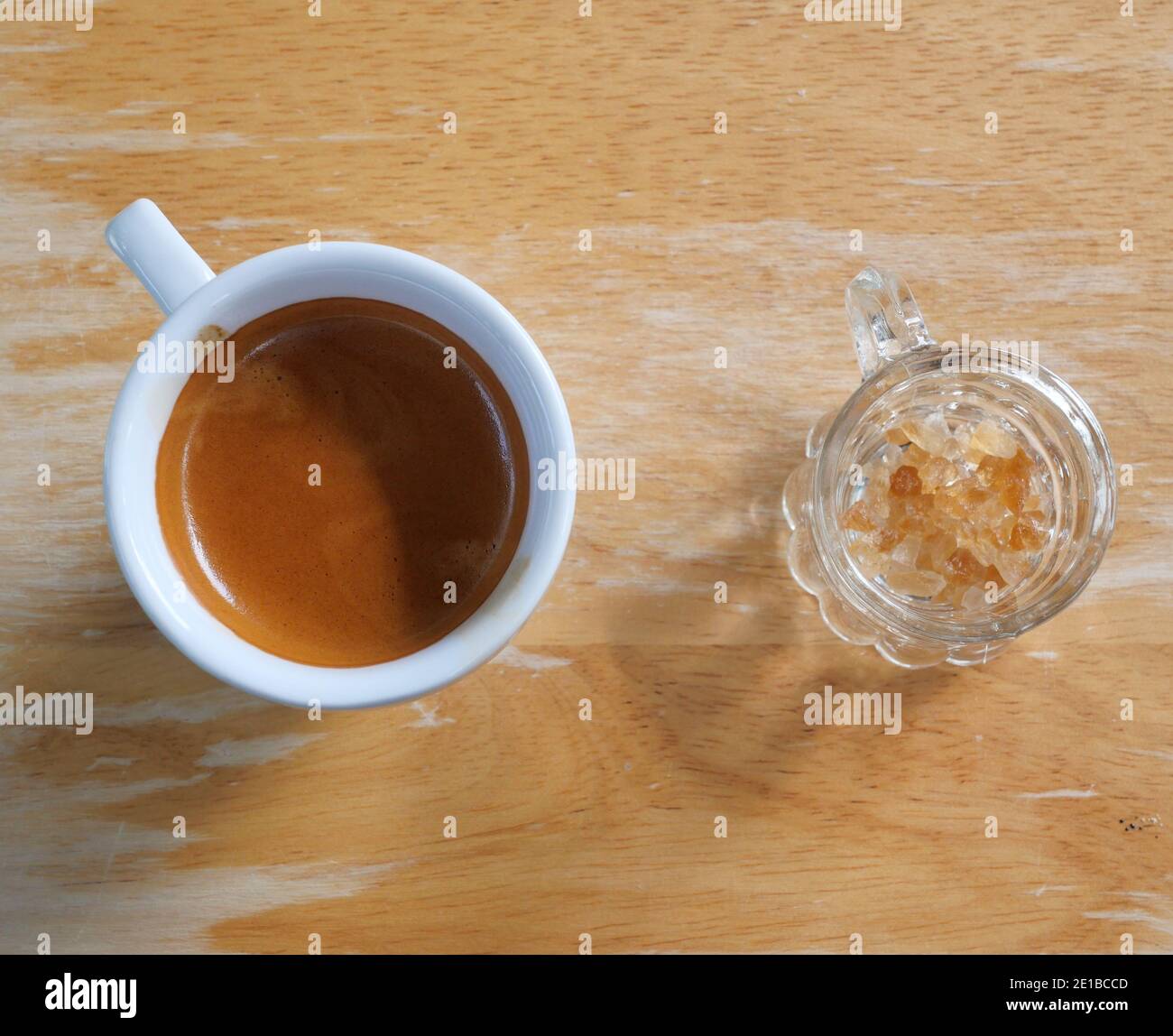 Caffè espresso in una tazza bianca con un bicchiere di zucchero di roccia, bevanda calda con tavolo di legno marrone sullo sfondo Foto Stock