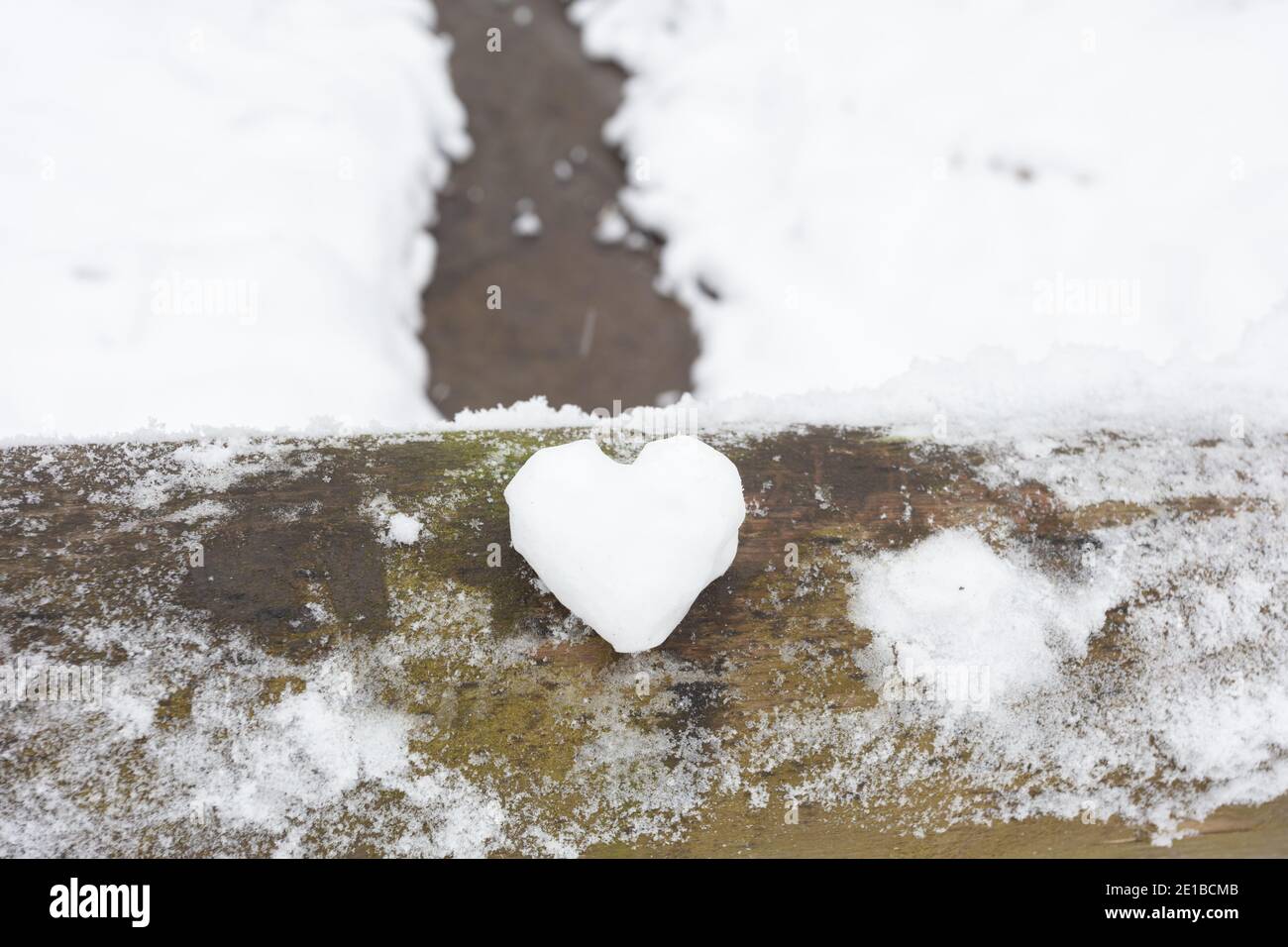 Un cuore fatto di neve si trova su una ringhiera in legno, sullo sfondo di un paesaggio invernale con un fiume. Foto di alta qualità Foto Stock