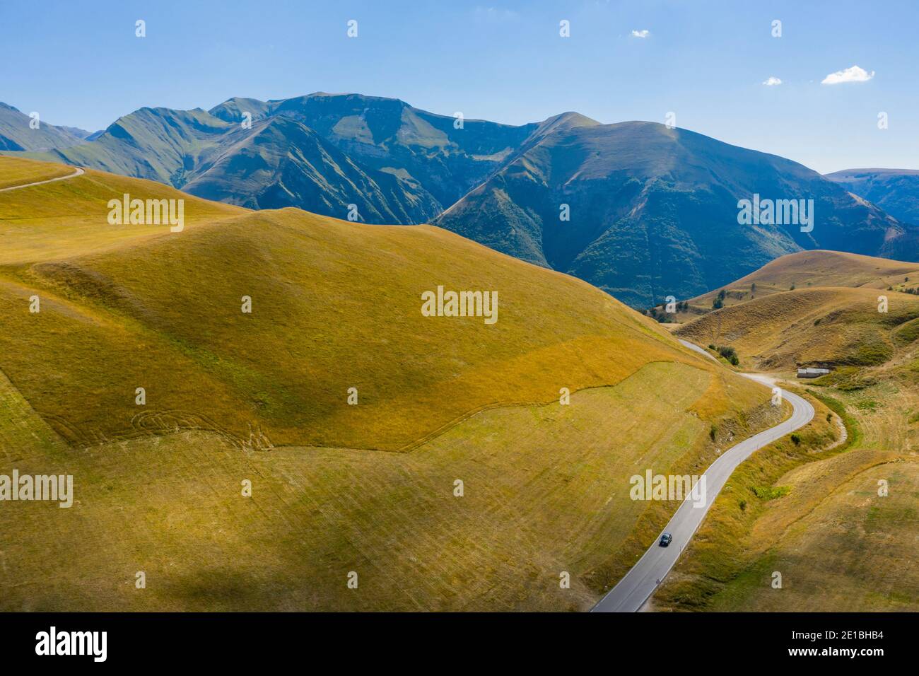 Un'auto passa per una strada solitaria a piani di Ragnolo, i Monti  Sibillini in Italia. Estate, sfondo con la catena montuosa degli Appennini  Foto stock - Alamy