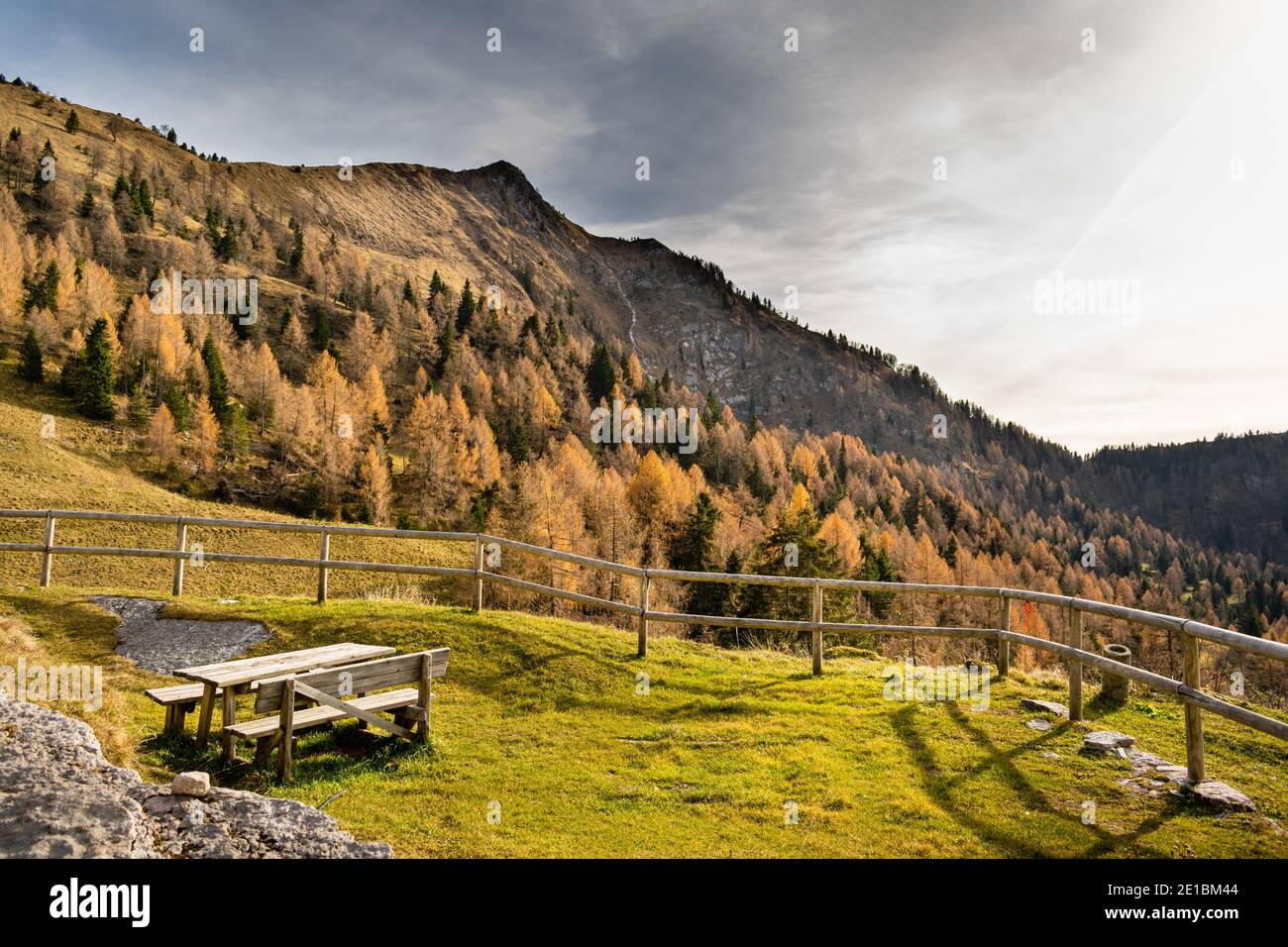 Panorama con cielo nuvoloso, montagne e pendii alberati. Nel tavolo in primo piano e panca di legno. Cesiomaggiore, Belluno, Italia Foto Stock