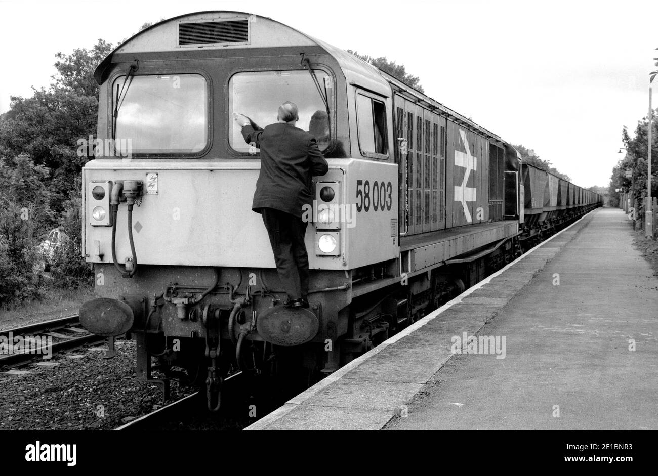 Il conducente pulisce il parabrezza della locomotiva diesel classe 58 n.58003 che dirige un treno MGR vuoto alla stazione di Warwick, Regno Unito. 9 giugno 1986 Foto Stock