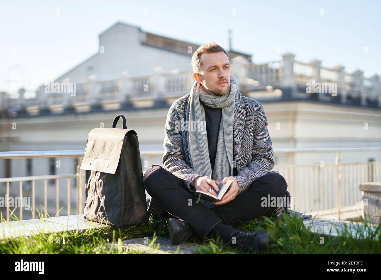 Uomo d'affari attraente in sciarpa grigia e cappotto seduto sul tetto e  pensare, tenendo note e penna. Concetto di lavoro o di studio Foto stock -  Alamy