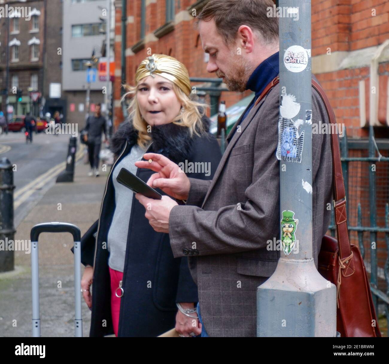 Donna con sciarpa d'oro sulla testa si alza accanto all'uomo con la sigaretta e il telefono in mano. Shoreditch, Londra est. Foto Stock