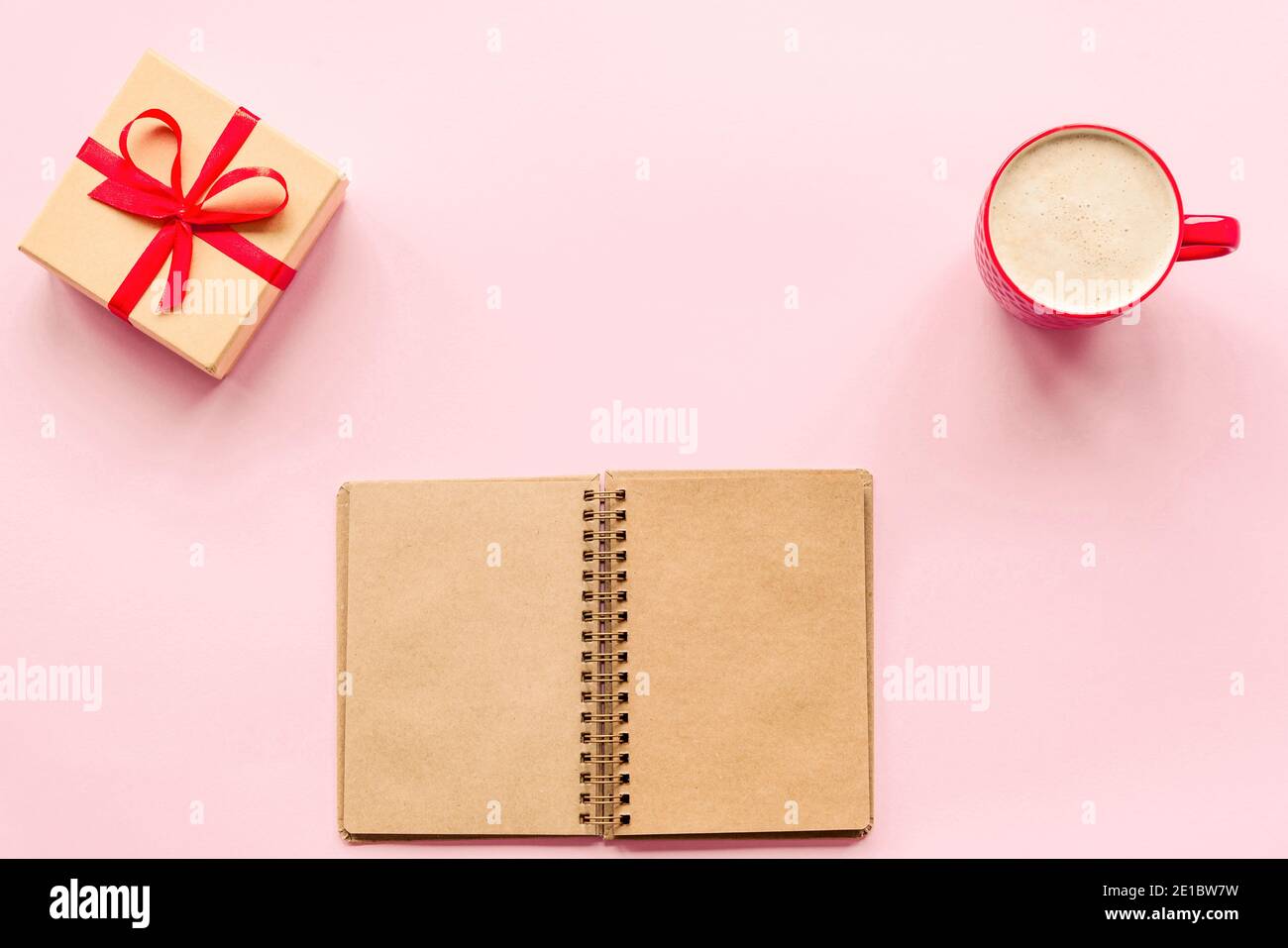 Tazza di caffè, regalo in una scatola e un notebook su sfondo rosa. Concetto di amore, giorno di San Valentino. Vista dall'alto, disposizione piatta. Foto Stock