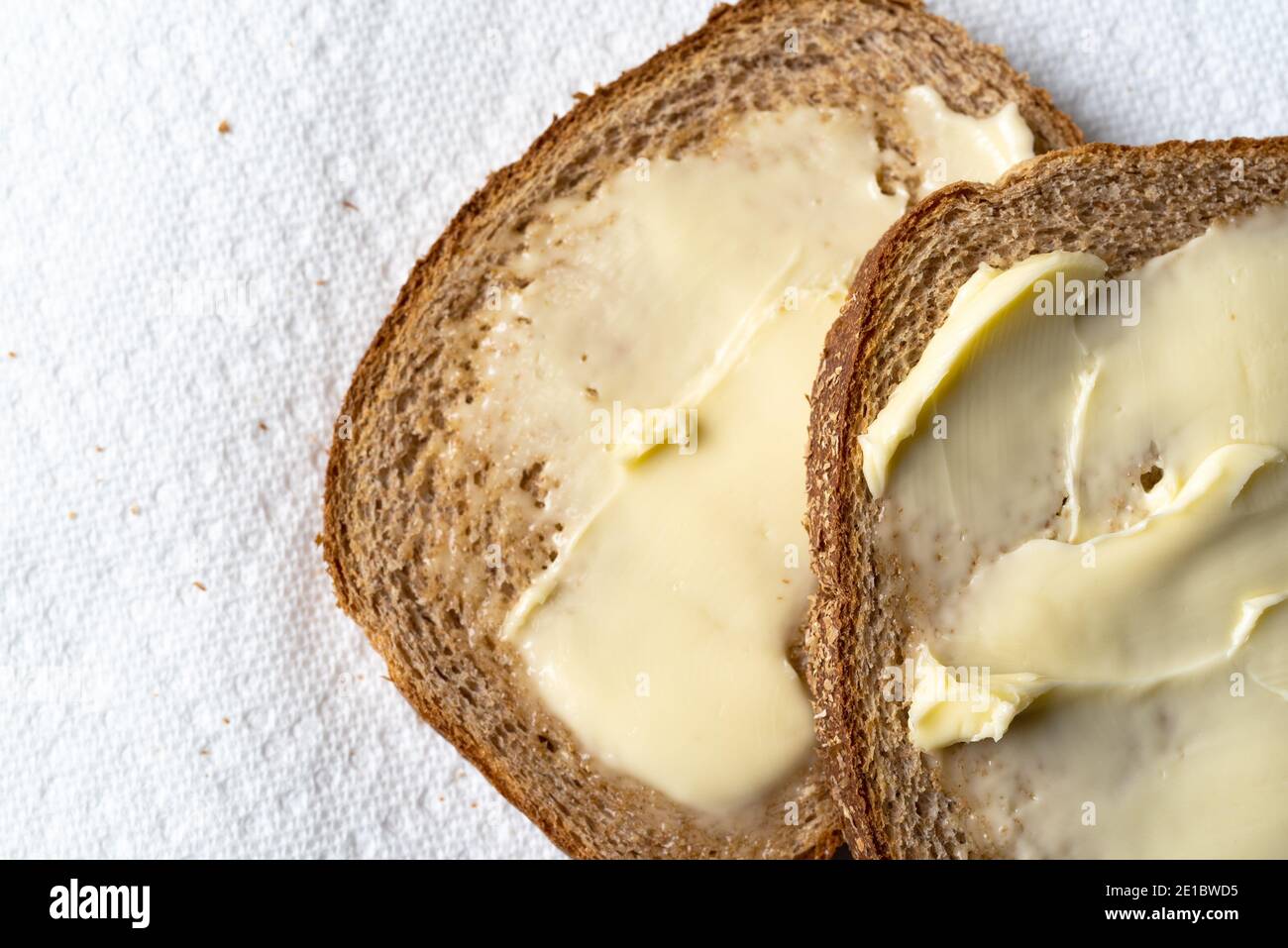 Vista ravvicinata dall'alto di due fette di pane di grano leggermente tostato con margarina su asciugamani di carta bianca con luce naturale. Foto Stock