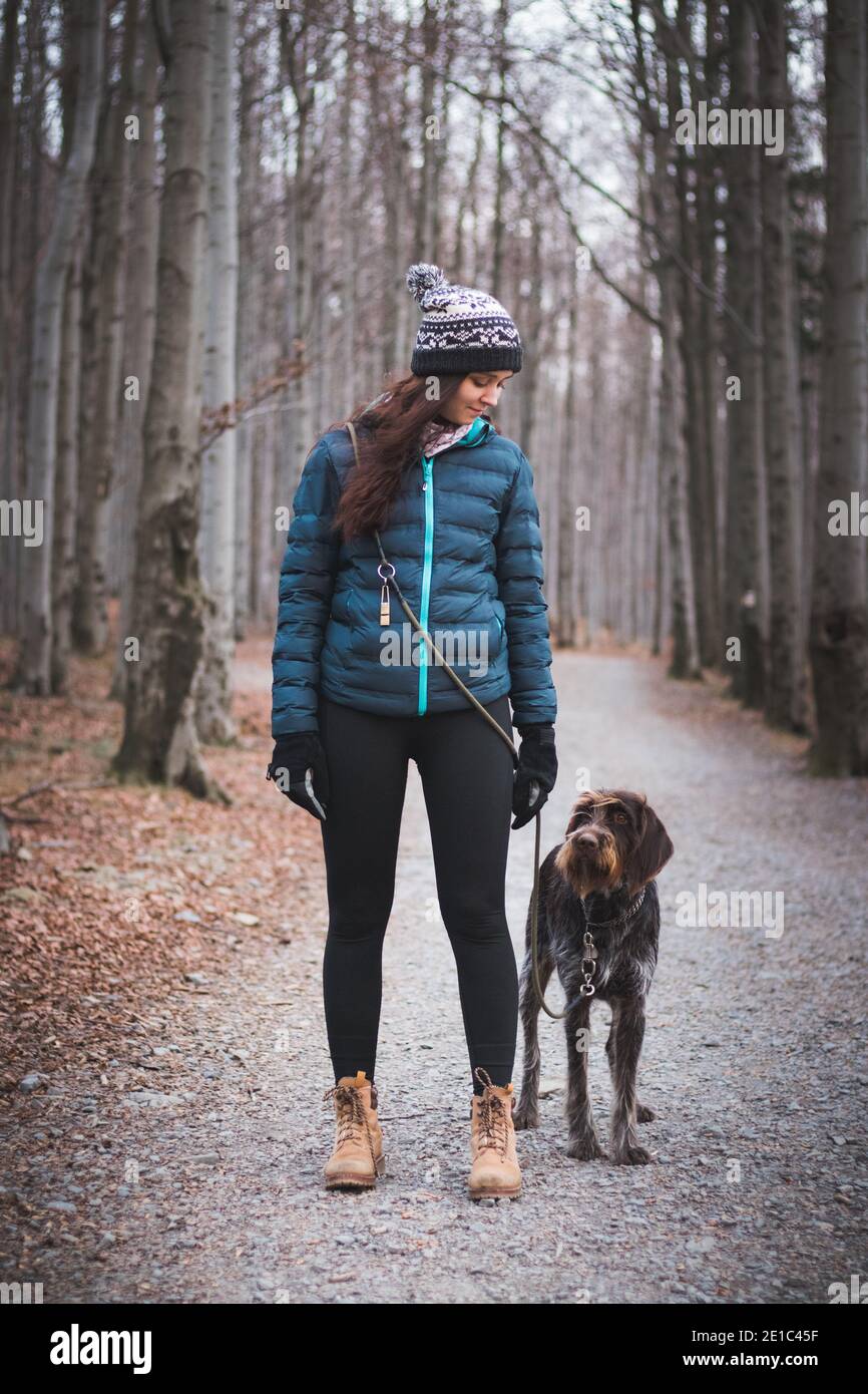 Giovane donna con il suo cane in bella foresta in una passeggiata mattutina. Collegamento tra un cane e una donna. Rapporto di fiducia reciproca. Donna con jacke blu Foto Stock