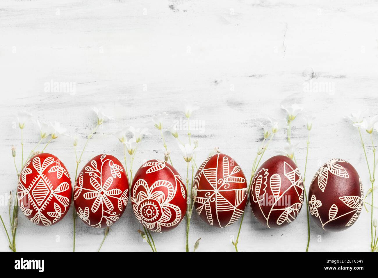 Fila di uova di Pasqua tinte a mano in cera rossa e bianca. Ucraino pysanka cornice su sfondo bianco legno con spazio copia per il testo Foto Stock