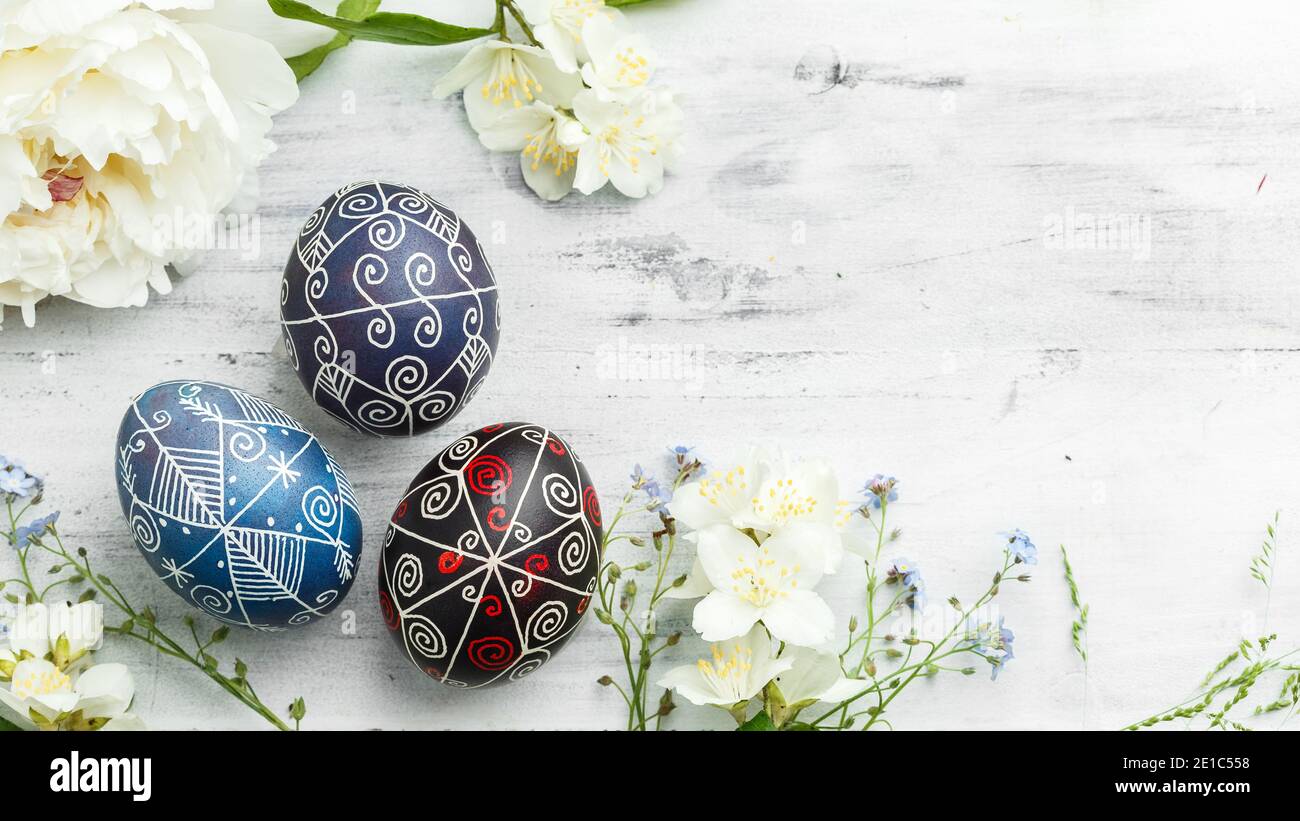 Tre uova di Pasqua dipinte a mano con fiori primaverili. Pysanka Ucraina decorata con tecnica di tintura cerata-resistente su sfondo bianco di legno shabby Foto Stock