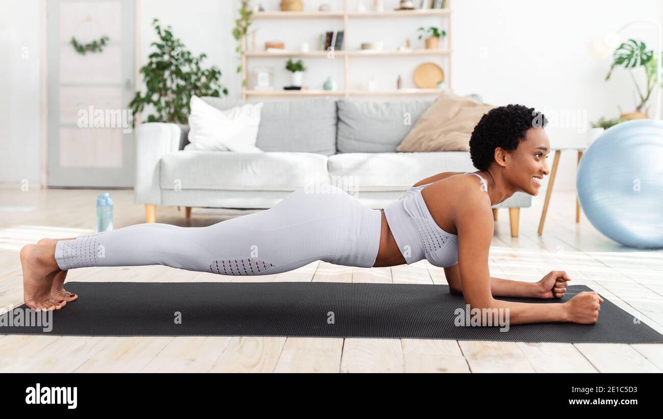 Allenamento domestico. Donna nera che si allenano sul tappeto yoga, facendo la posizione del gomito, rinforzando i muscoli abs Foto Stock
