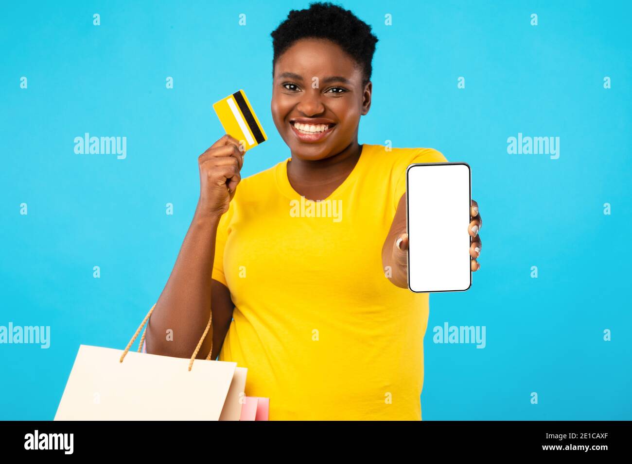 Donna africana che mostra schermo del telefono e carta di credito, sfondo blu Foto Stock