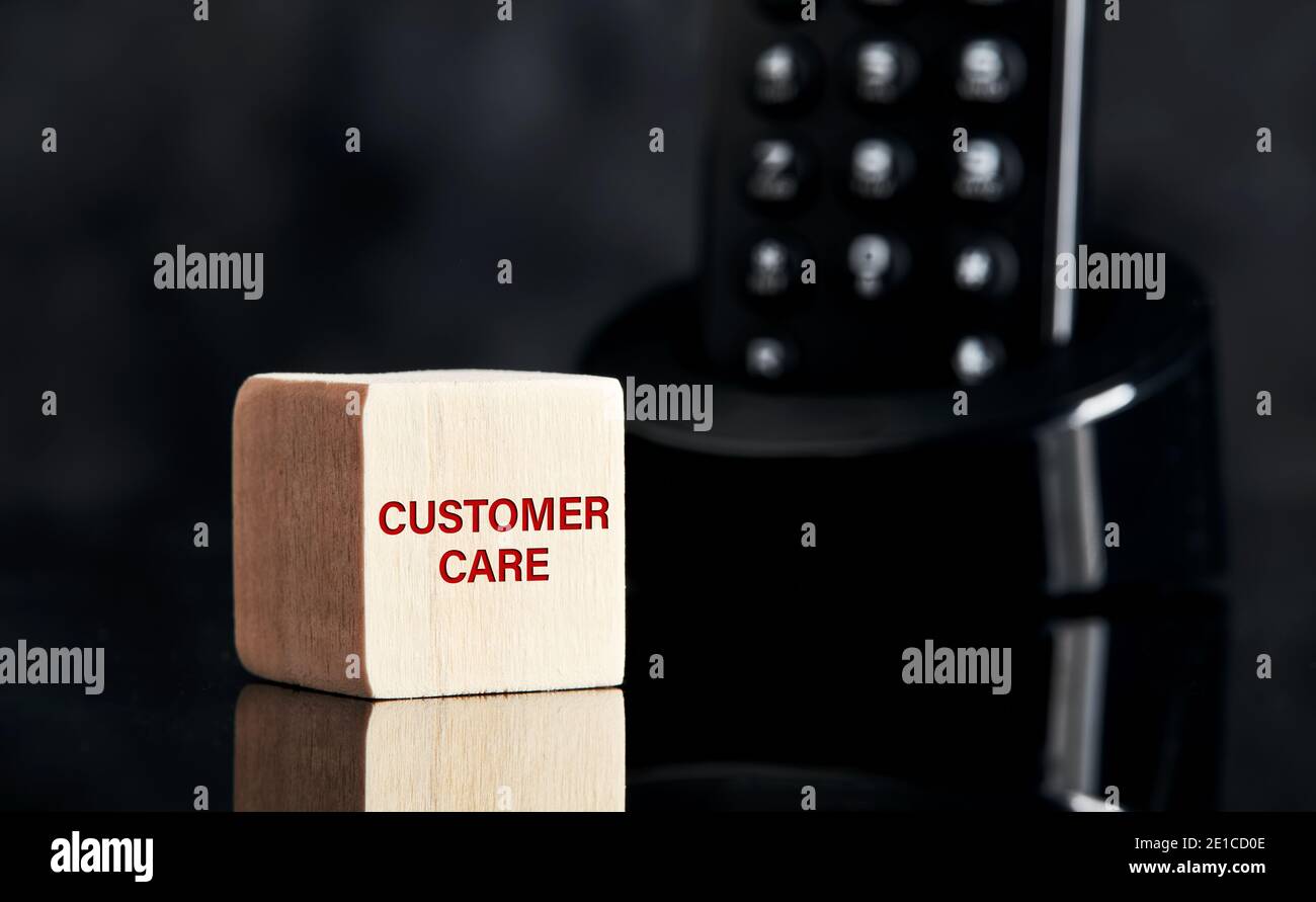 La parola Customer Care su blocco di legno con sfondo telefonico. Concetto aziendale per la guida, il supporto, l'assistenza o l'assistenza tecnica. Foto Stock