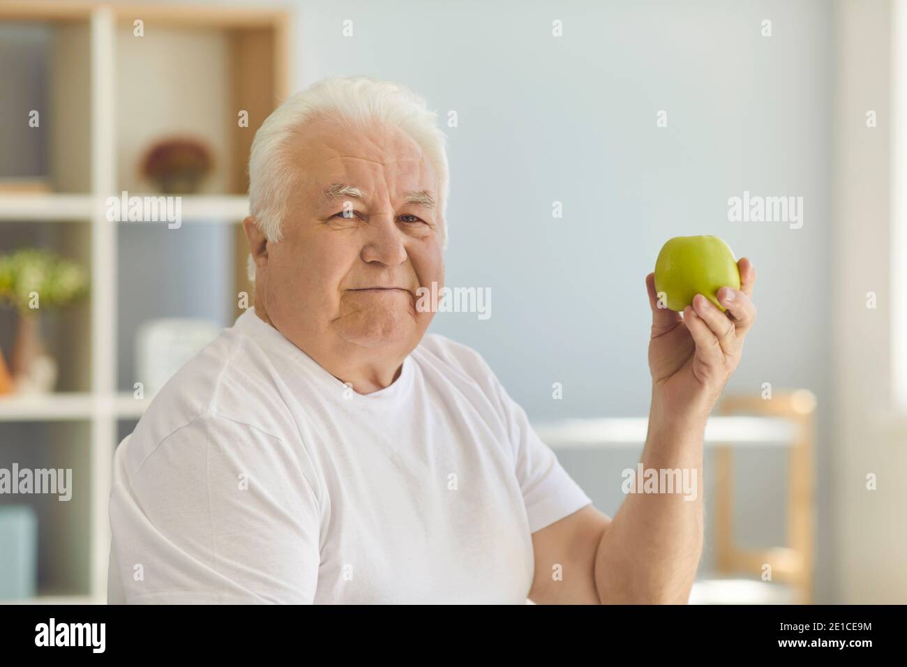 Uomo anziano che tiene la mela verde e raccomanda di mangiare la frutta cruda e mantenere una dieta sana Foto Stock