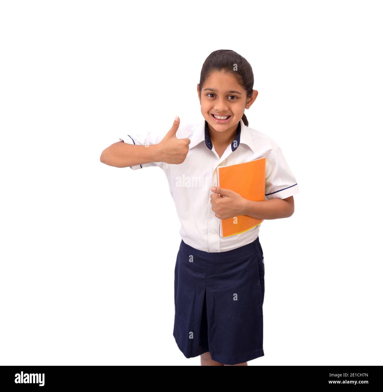 Ritratto di una ragazza indiana felice di scuola indossare uniforme sorridente e mostrando pollici verso l'alto gesto della mano e raffigurante la vittoria. Foto Stock