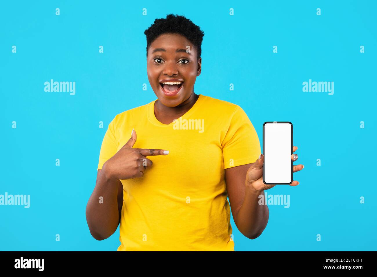 Ecited Black Woman che punta sullo schermo del telefono su sfondo blu Foto Stock