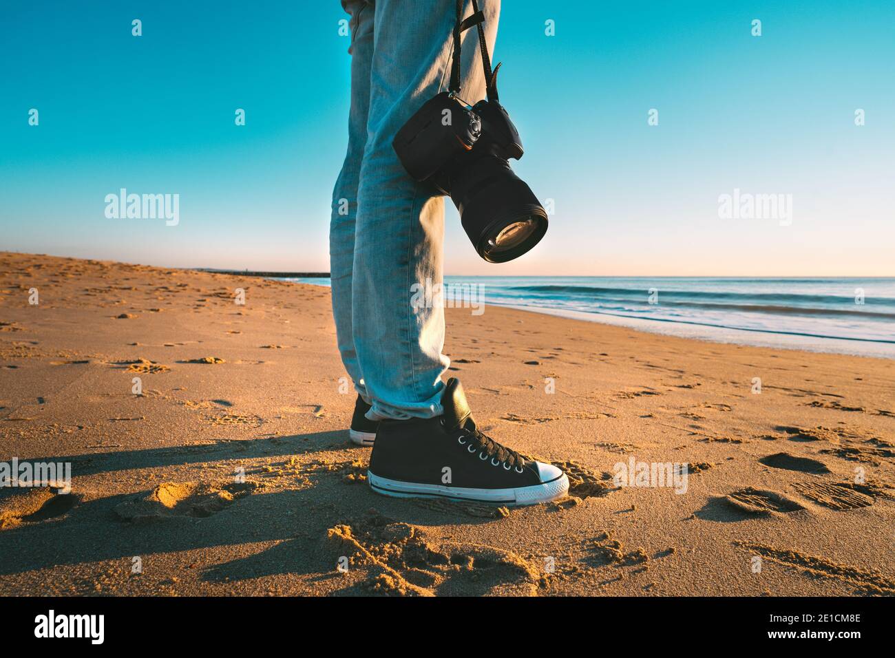 Fotografo professionista con la sua macchina fotografica sulla spiaggia al tramonto. Fotografia in spiaggia. Pronto per scattare foto al tramonto Foto Stock