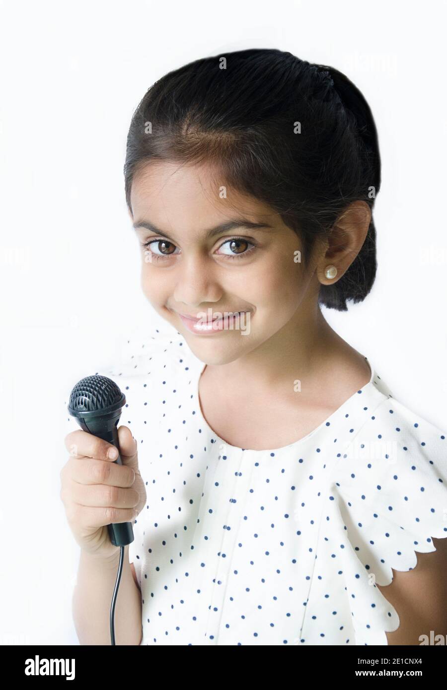 Bel ritratto di un bambino indiano sorridente che tiene in posa cantando con un microfono vestito di bianco. Foto Stock