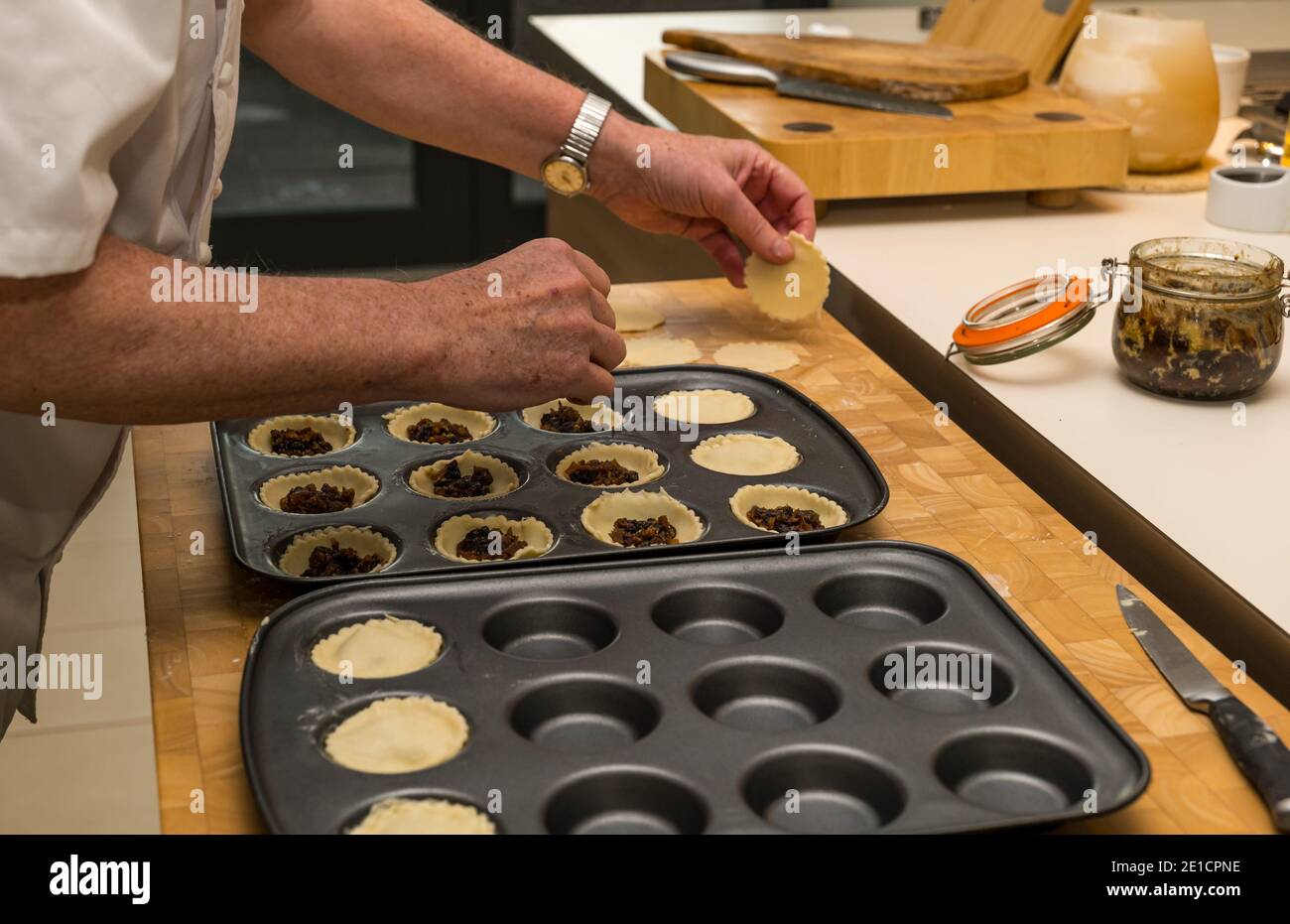 Mani dell'uomo che riempiono le casse di pasta in tini da forno con la carne macellata Per fare torte mince al tempo di Natale Foto Stock
