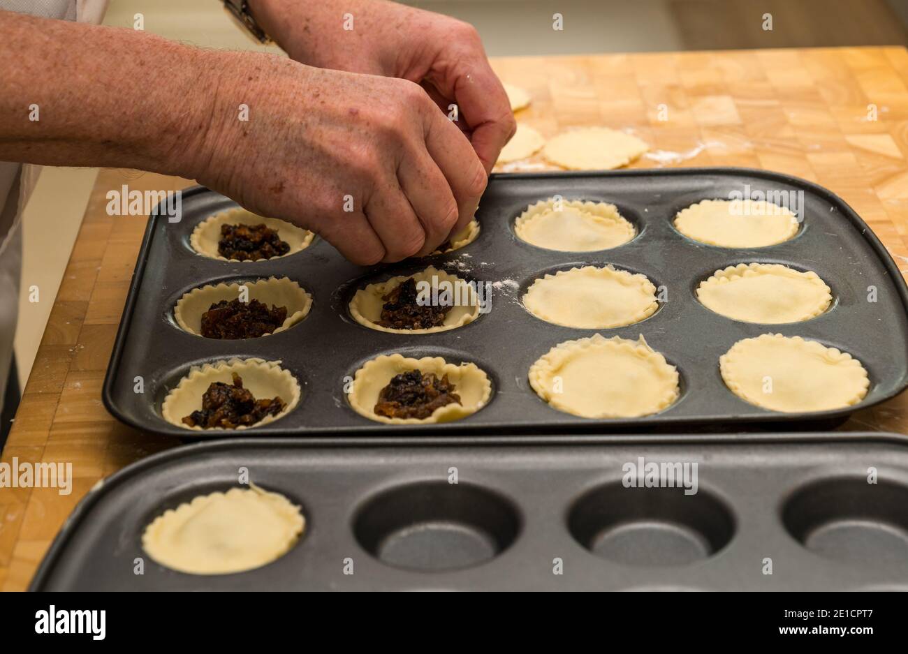 Mani dell'uomo che riempiono le casse di pasta in tini da forno con la carne macellata Per fare torte mince al tempo di Natale Foto Stock