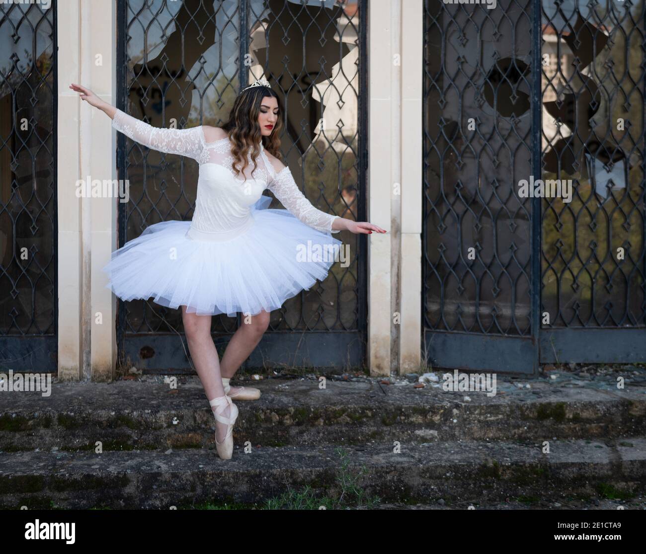 Ragazza ballerina adolescente che indossa abiti bianchi e scarpe da ballo punta fuori di una casa abbandonata Foto Stock