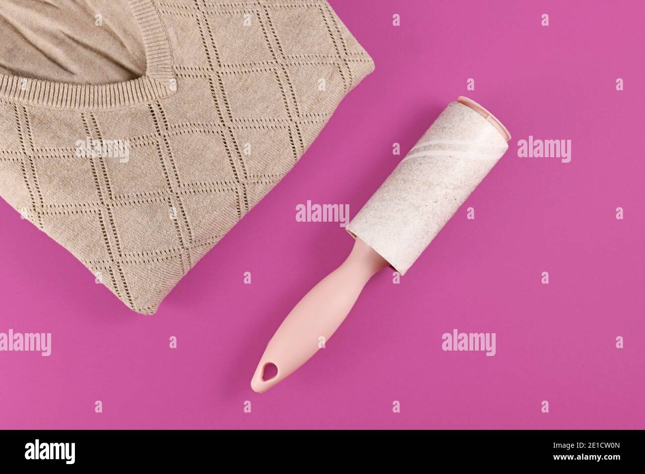 Rullo di lanugine usato accanto al maglione piegato su rosa scuro sfondo Foto Stock