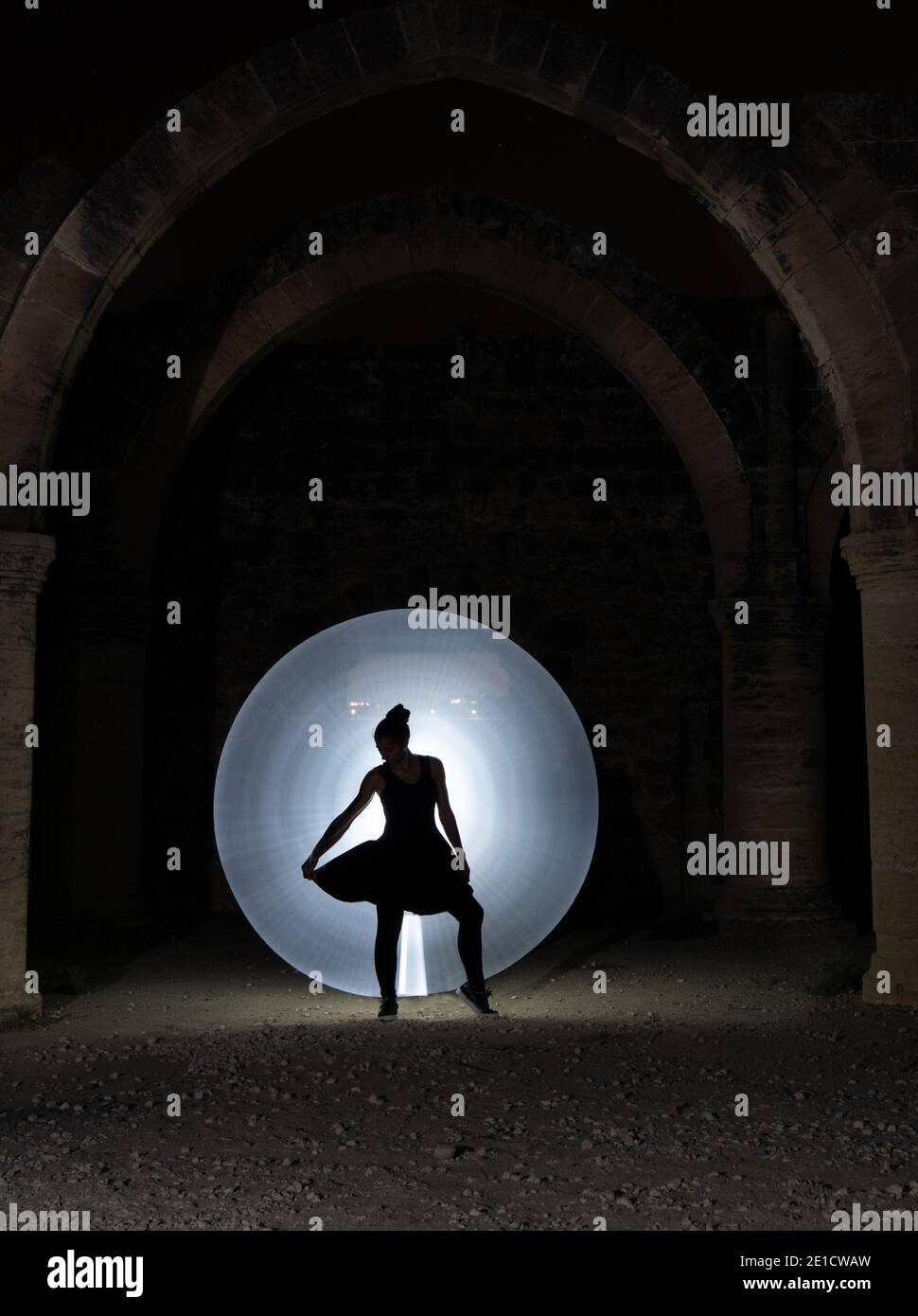 Giovane donna che danzava sotto una vecchia colonna lapidata con un cerchio di luce di pittura dietro. Fotografia di pittura leggera Foto Stock