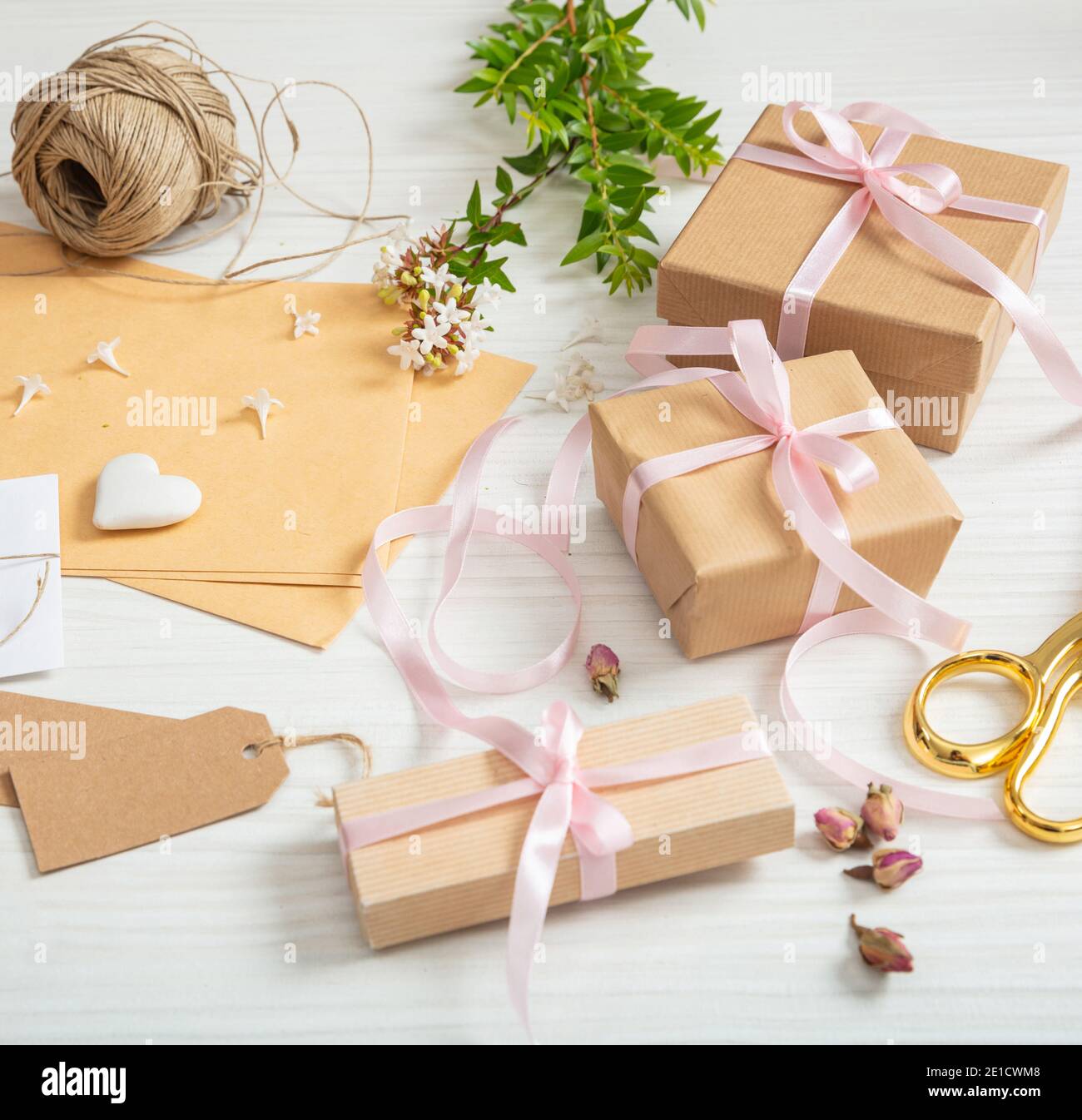 Le scatole di regalo e gli inviti sono appoggiati su un piano di legno  bianco. Vista dall'alto di confezioni presenti fatte a mano, etichette  marroni vuote, carta da imballaggio per kraft, ri