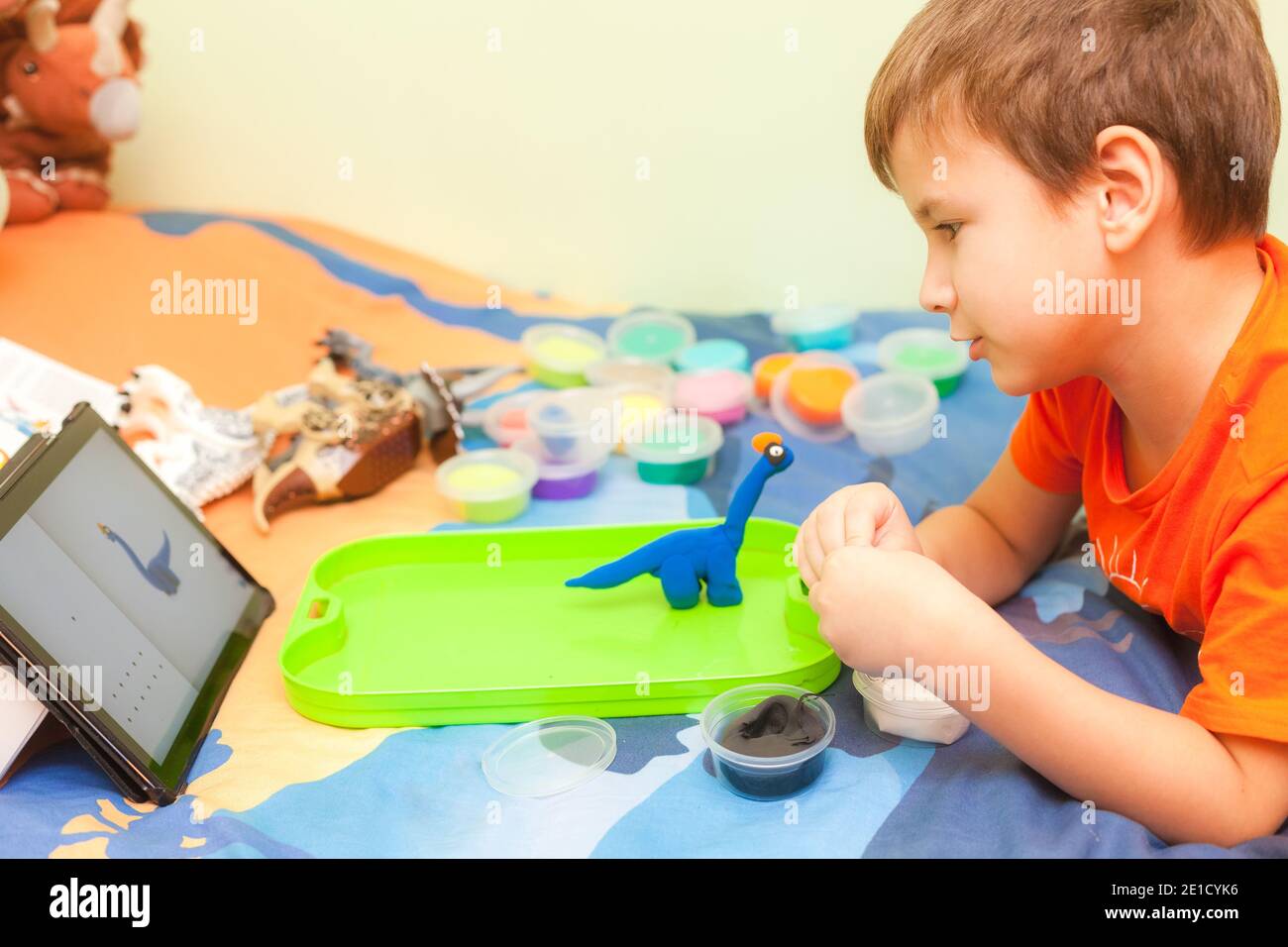 Cute 7 anni ragazzo sculpts brachiosaurus da plastilina su il suo letto in camera per bambini Foto Stock