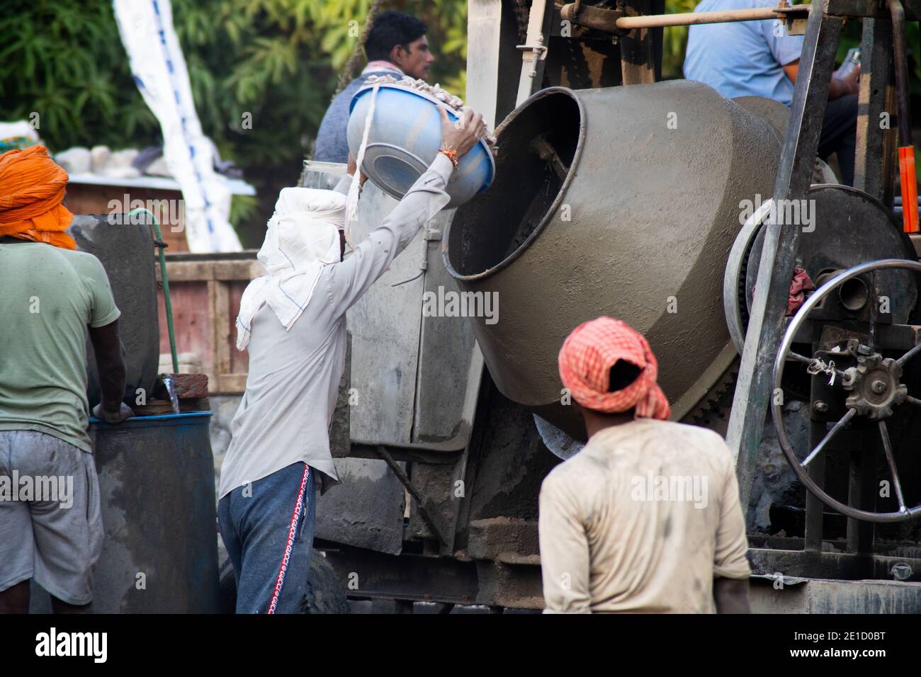 zoomed in colpo di operai di costruzione underprived indiani che trasportano la sabbia, il cemento, le pietre e l'acqua sulla loro testa per caricare in un miscelatore per fare Foto Stock