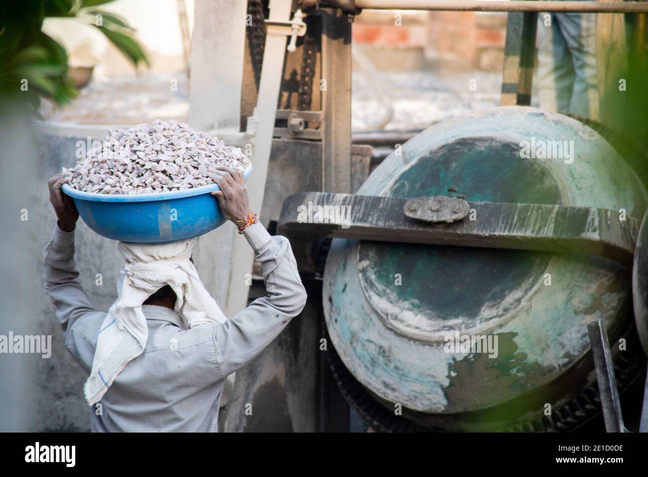 zoomed in colpo di operai di costruzione underprived indiani che trasportano la sabbia, il cemento, le pietre e l'acqua sulla loro testa per caricare in un miscelatore per fare Foto Stock