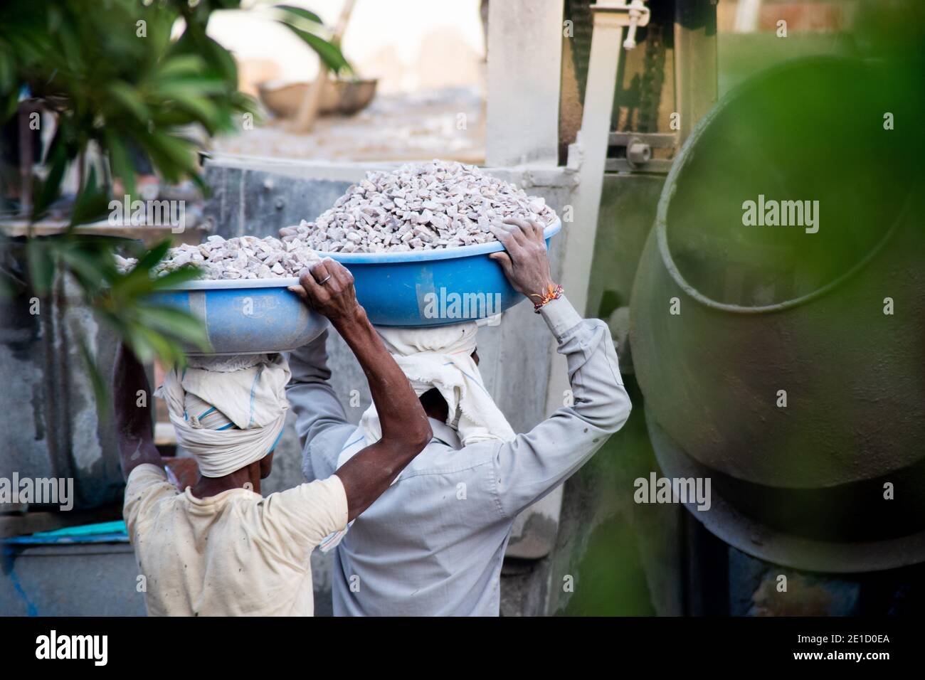 zoomed in colpo di operai di costruzione underprived indiani che trasportano la sabbia, il cemento, le pietre e l'acqua sulla loro testa per caricare in un miscelatore per fare Foto Stock