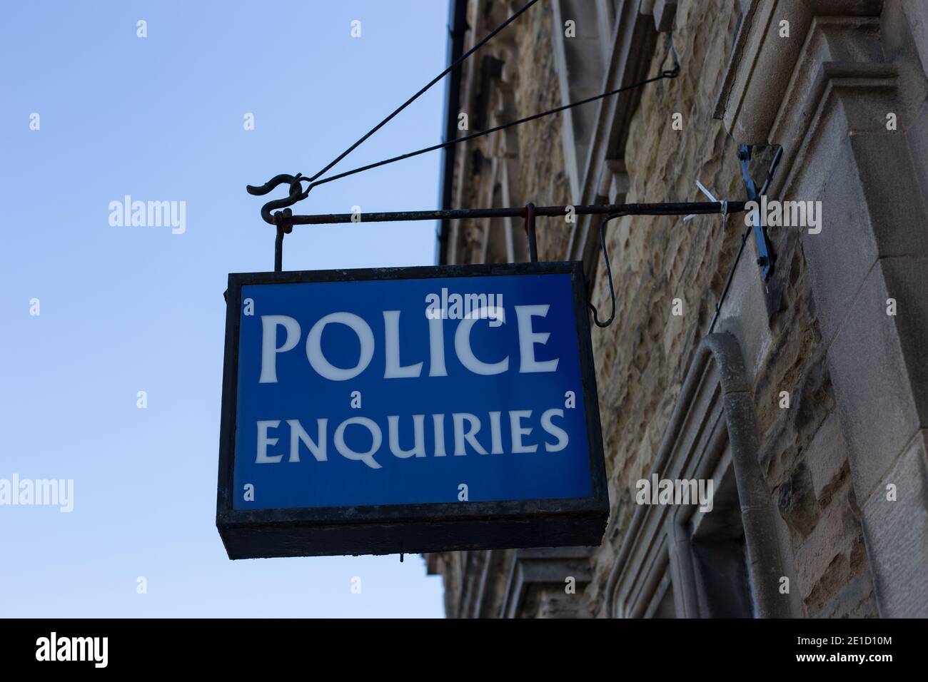 Un vecchio cartello blu illuminato di informazioni pubbliche 'Police Enquiries' appeso fuori della stazione di polizia a Leyburn, North Yorkshire, Inghilterra Foto Stock