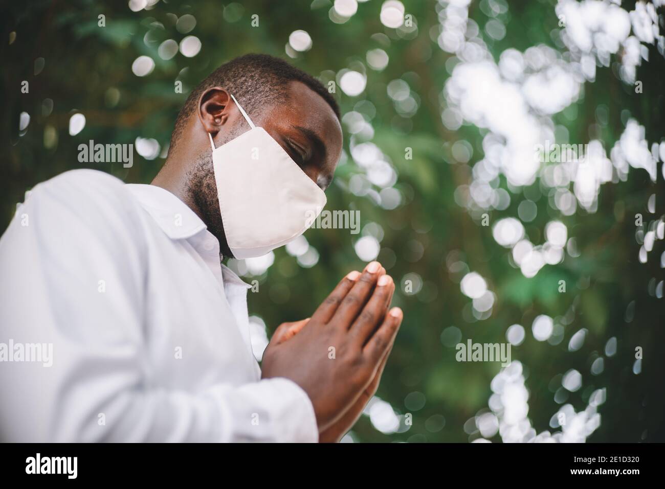 Uomo africano che prega per dio con maschera di indossare il viso Foto Stock