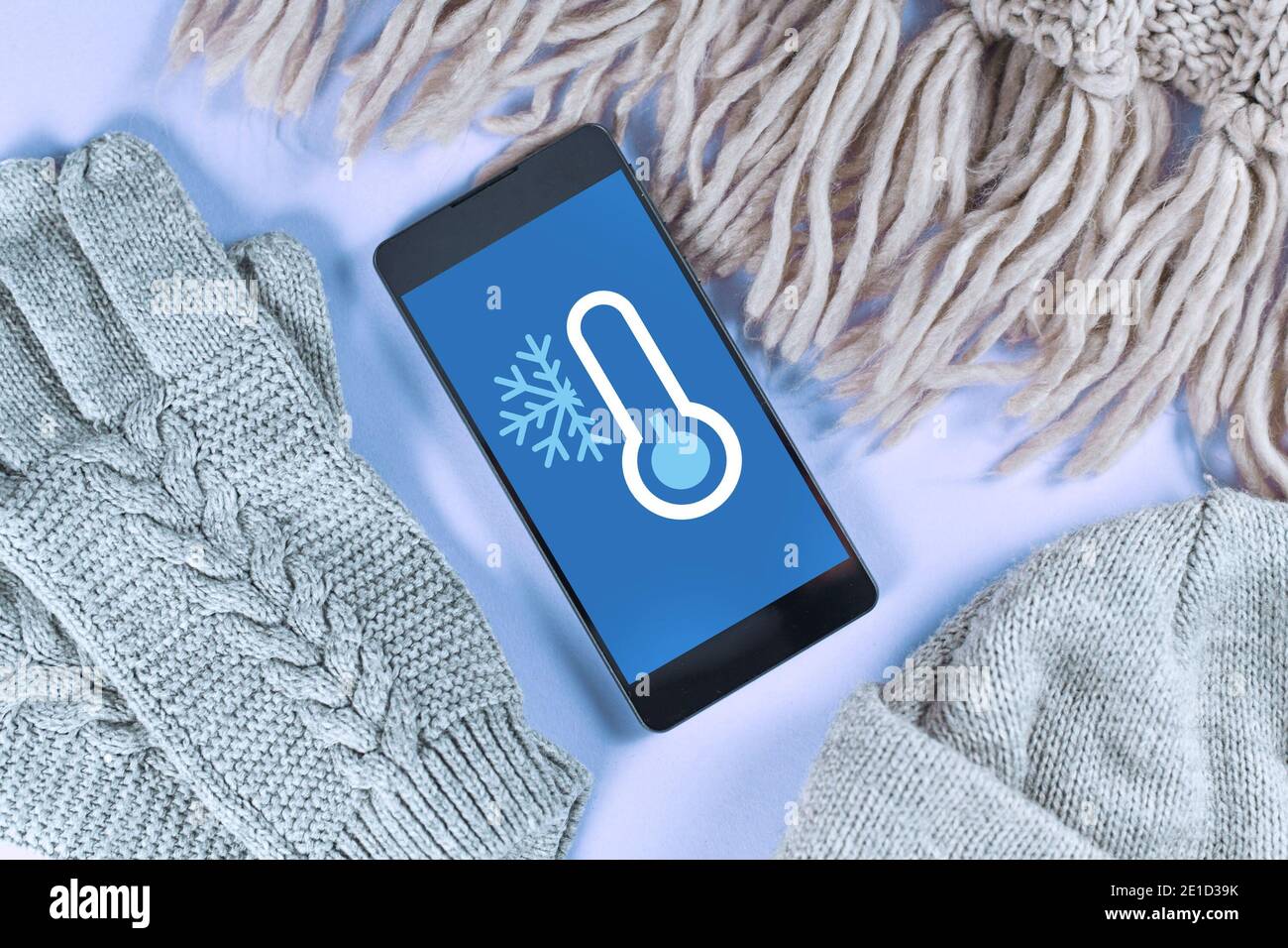 Concetto per temperature basse con neve e meno gradi con telefono cellulare con previsioni meteo circondato da abiti caldi invernali come la sciarpa Foto Stock