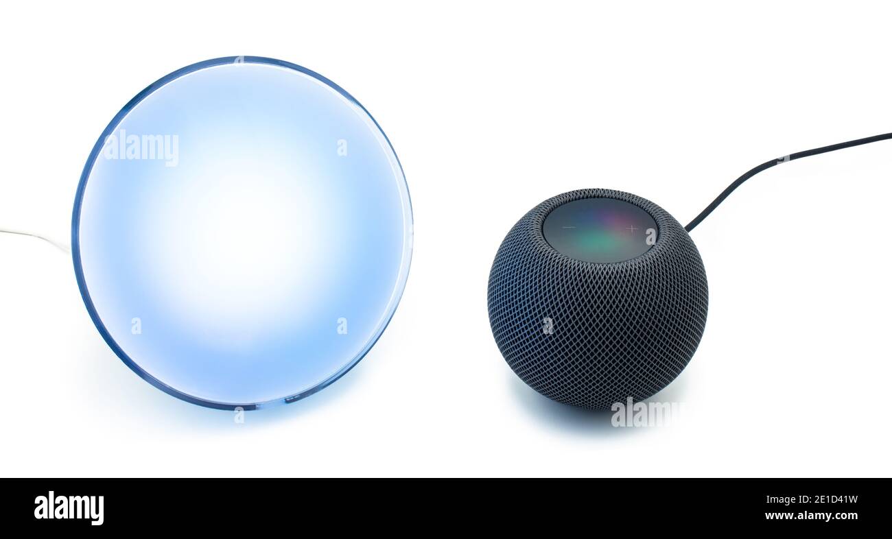 Siri, il controllo vocale del nuovo altoparlante nero intelligente Apple HomePod Mini, viene utilizzato per controllare una lampada domestica intelligente Philips hue su uno sfondo bianco chiaro Foto Stock