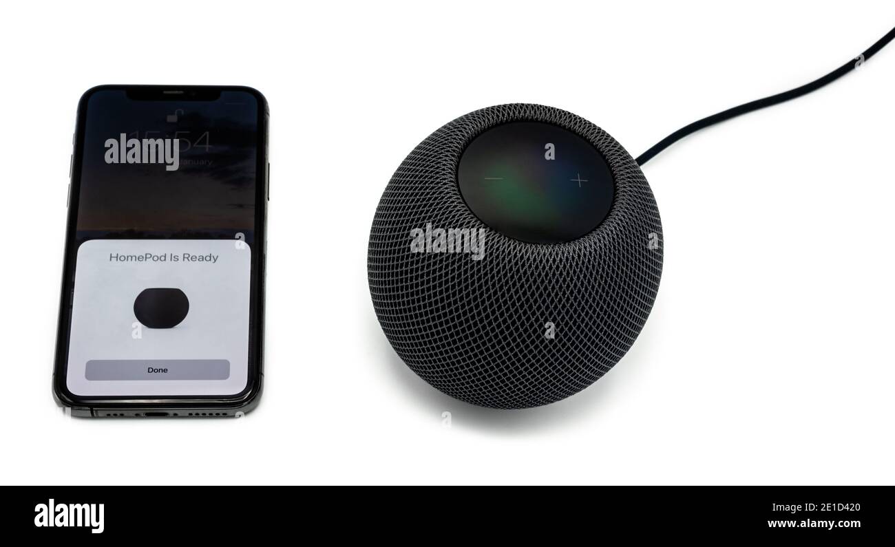 Un altoparlante nero Apple HomePod Mini Smart viene configurato utilizzando un Apple iPhone 12, girato in studio con ombre su uno sfondo bianco chiaro. Foto Stock