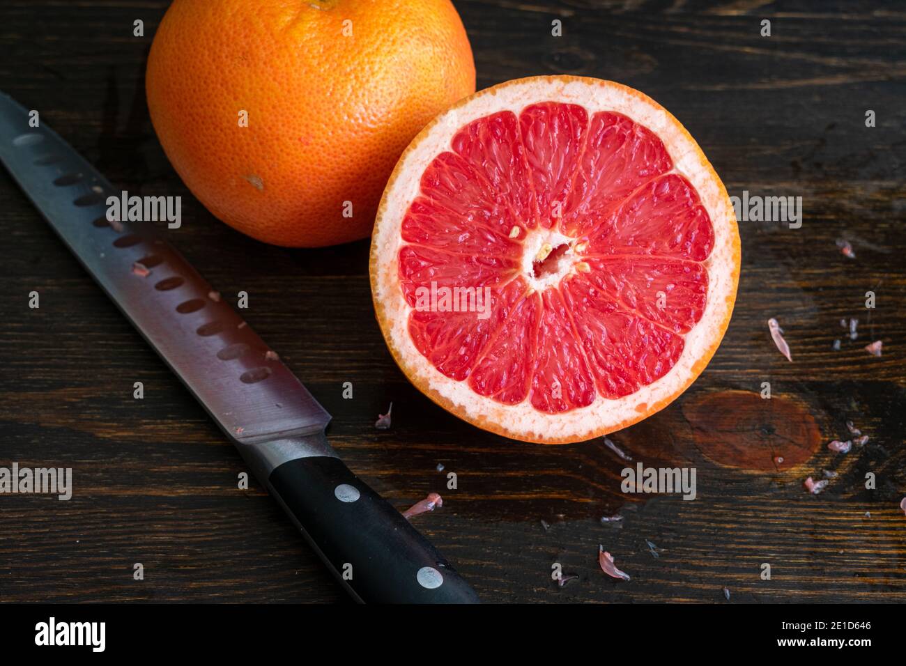 Pompelmo rosso tagliato a metà: Pompelmo rosa intero e dimezzato su un tagliere di legno scuro Foto Stock