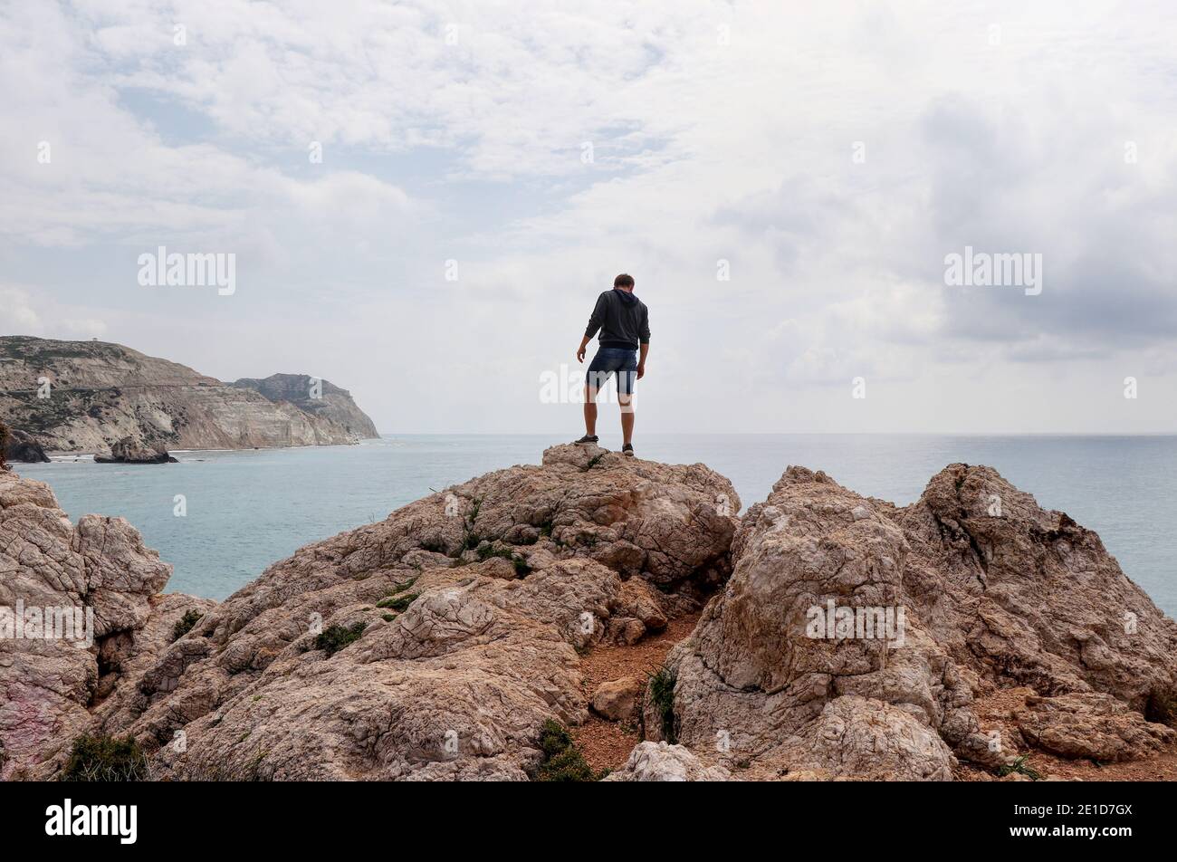 Il giovane si erge sulla cima di una collina rocciosa nel mezzo del mediterraneo. Vista sull'oceano e le scogliere in lontananza. Famoso e bellissimo posto a Cypru Foto Stock
