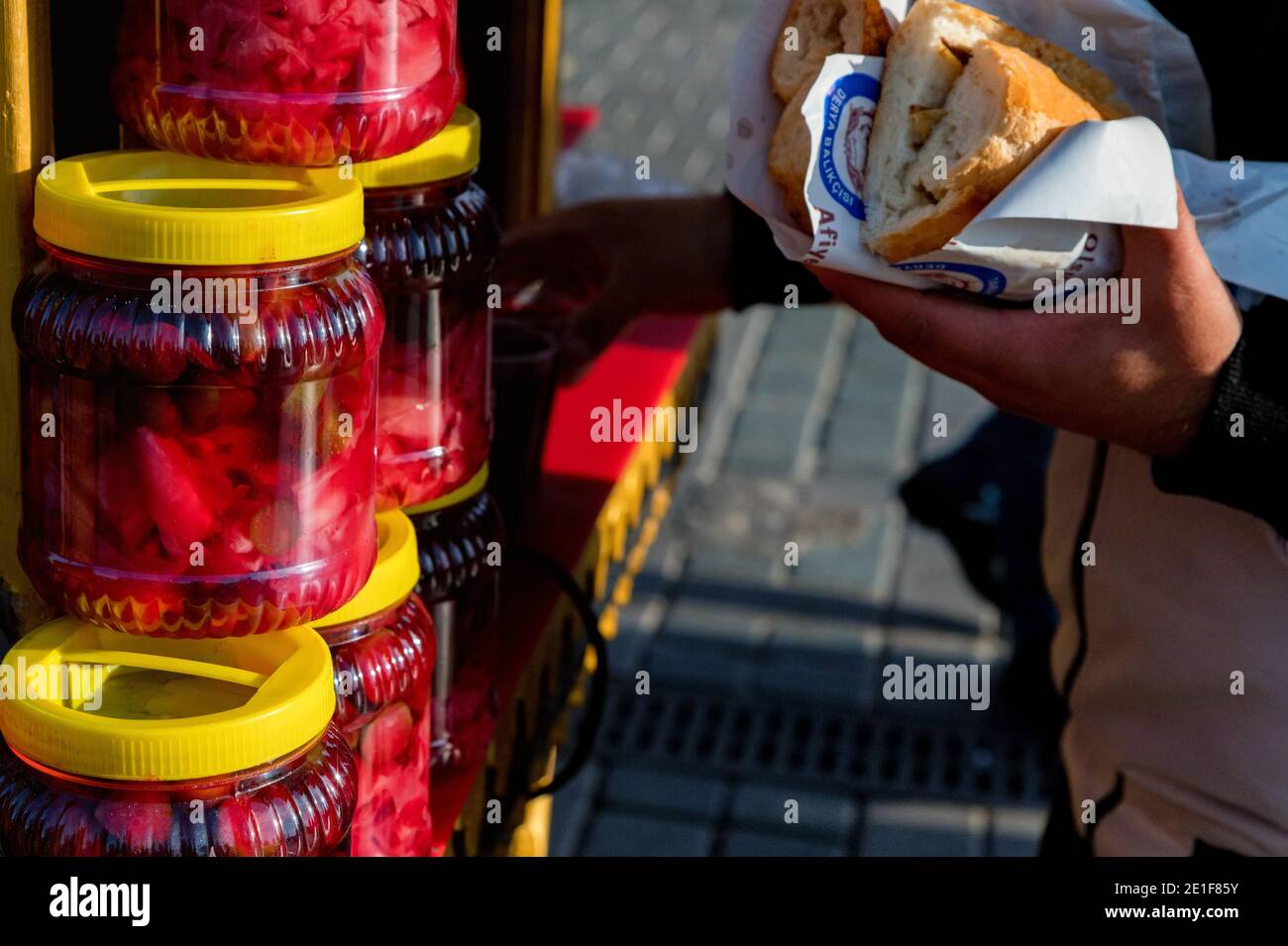 ISTANBUL, TURCHIA - 9 DICEMBRE 2020: Vasetti di vetro con diversi alimenti sottaceto sul mercato turco e panino per mani umane. Turco fast food concep Foto Stock