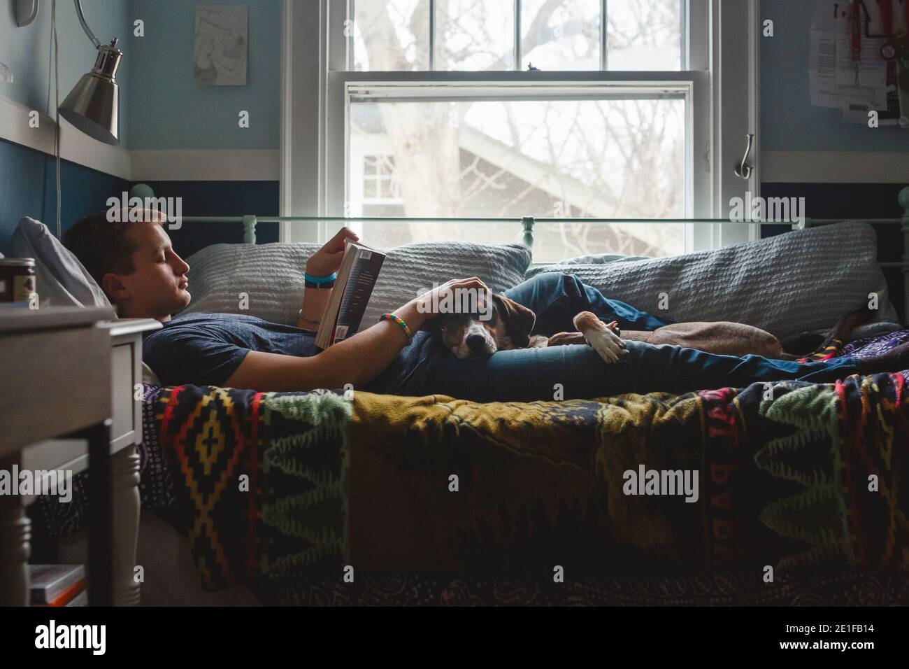Un giovane uomo si stende sul letto che accarezza il cane nel suo giro e leggere un libro Foto Stock