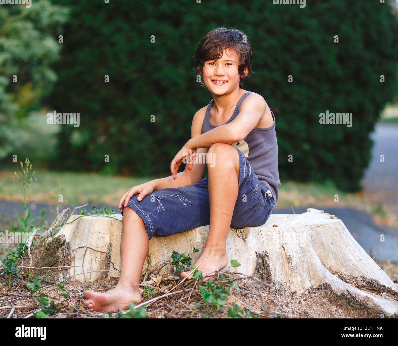 ritratto di felice ragazzo a piedi nudi con pelle dorata seduta moncone dell'albero Foto Stock