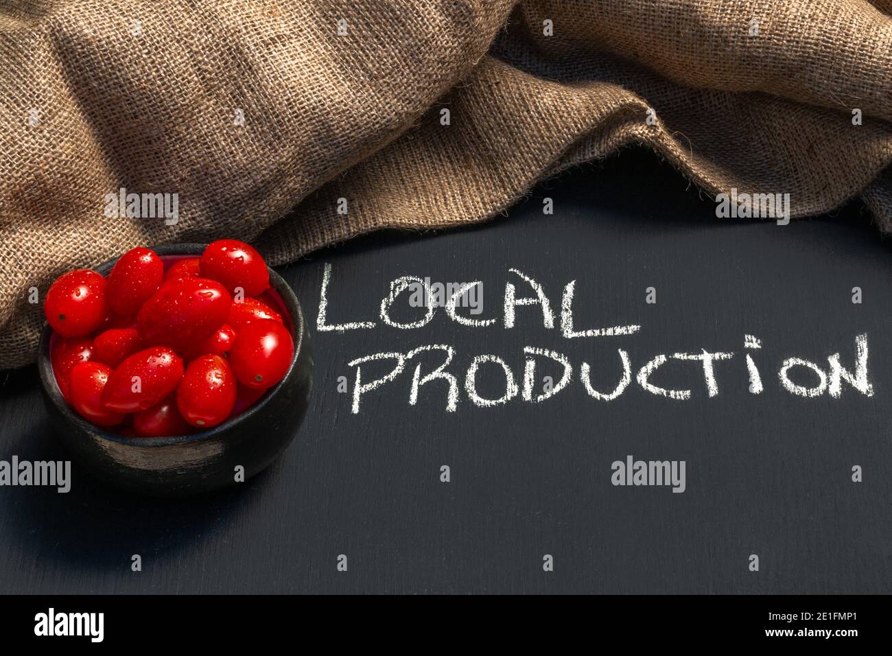 divertente colpo di lavagna con frase produzione locale con una ciotola di leggere pomodori ciliegini vibranti e sani, concetto sano fresco locale produrre la vena Foto Stock