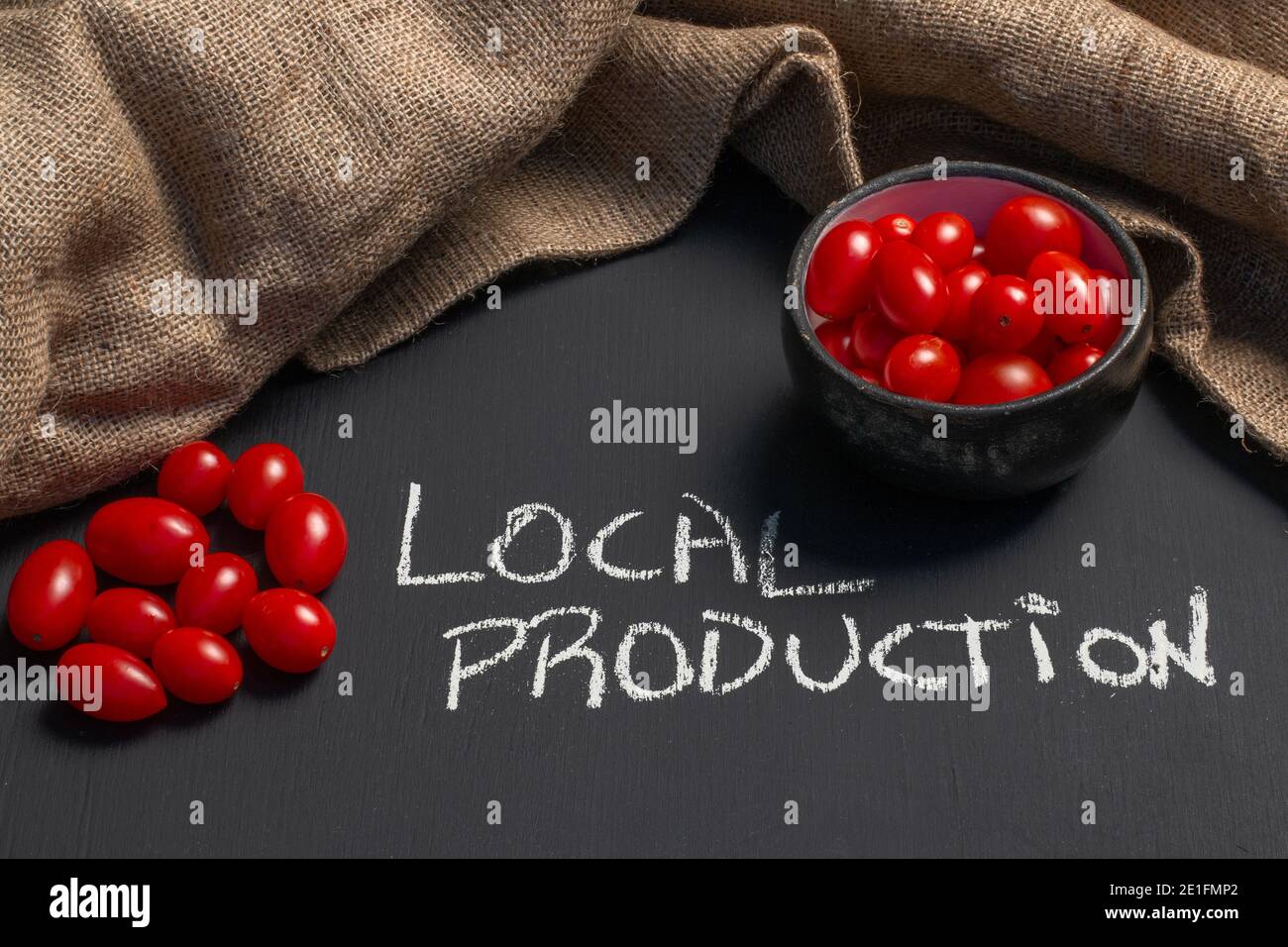 bel colpo di vibranti pomodori ciliegini freschi su una lavagna con la frase produzione locale scritta con gesso, concetto di mangiare fresco sano Foto Stock