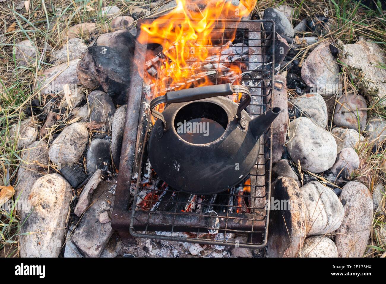 un bollitore con acqua calda sopra il fuoco. Teiera antica su pietre sulla griglia sopra il fuoco per la preparazione di tè o caffè outdoor.A speciale focolare per esterno. Foto Stock