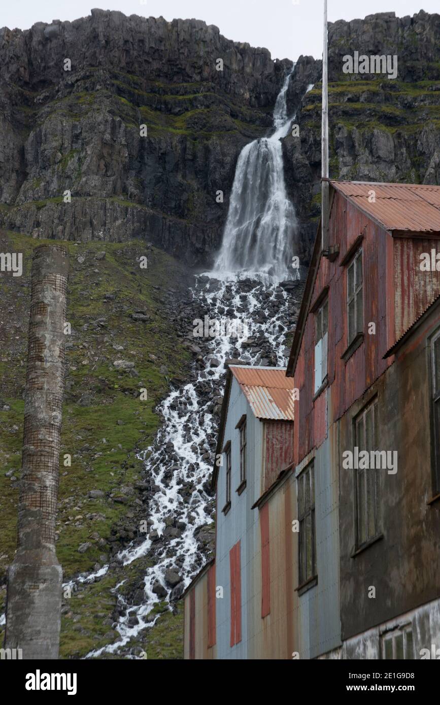 Cascata, camino in cemento e resti della vecchia fabbrica di aringhe, Djupavik, fiordi occidentali, Islanda Foto Stock