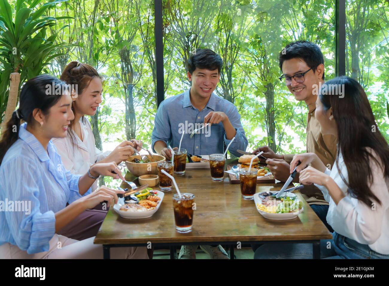Felice amico asiatico mangiare al ristorante. Amico di gruppo allegro compagni ridere gustando il pasto divertendosi seduti insieme al tavolo da pranzo del ristorante Foto Stock